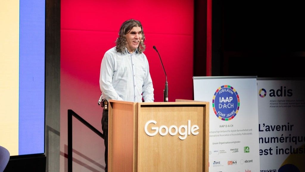 René Jaun am Podium. Er hat ein weisses Hemd an und spricht ins Mikrofon.