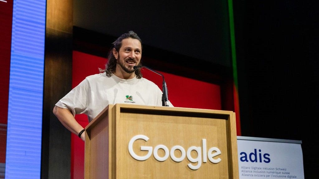 Mischa Bitterli steht am Rednerpult. Die Arme eingestützt in der Taille. Er lächelt.