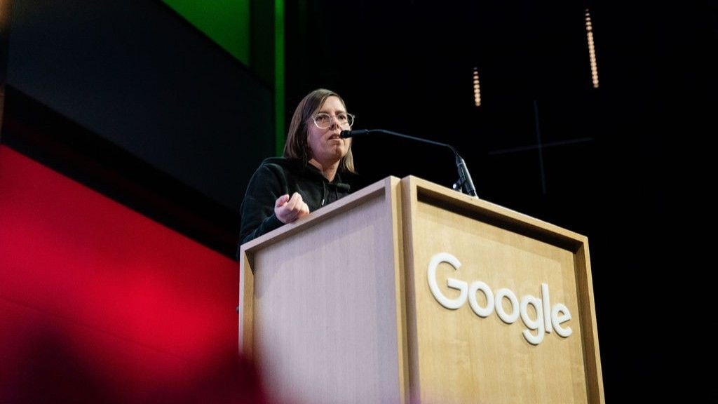 Simone Russi au pupitre. Elle parle au micro. La perspective de la photo permet de voir le logo Google en grand, visible à l'avant du pupitre.