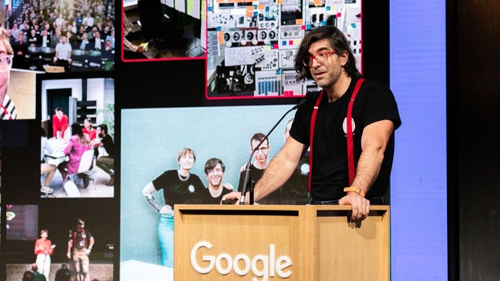 Stefan Barac è in piedi al podio. Parla appoggiandosi con entrambe le mani al podio. Sullo sfondo si vedono molte foto della sua conferenza.